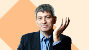 Photo of Carl Zimmer, columnist for The New York Times. He is wearing a navy suit and holding his hand up.